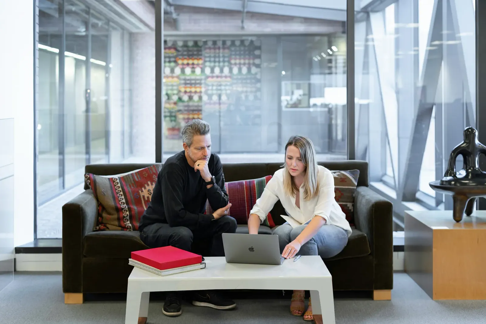 Ein Mann und eine Frau sitzen auf einem Sofa in einer modernen Lobby und arbeiten gemeinsam an einem Laptop