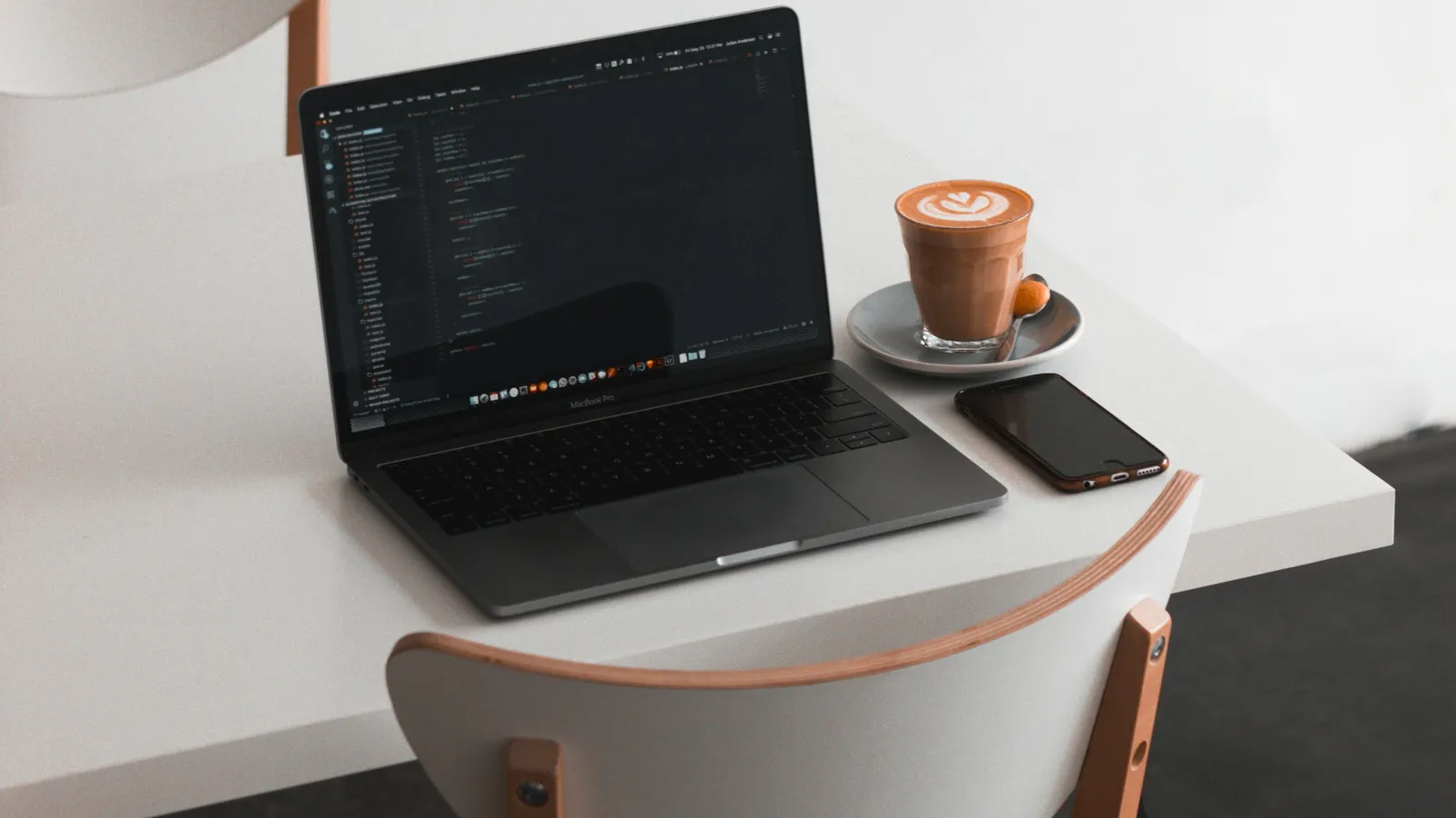 Aufgeklappter Laptop mit Programmcode auf einem hellen Schreibtisch, daneben eine Tasse Kaffee